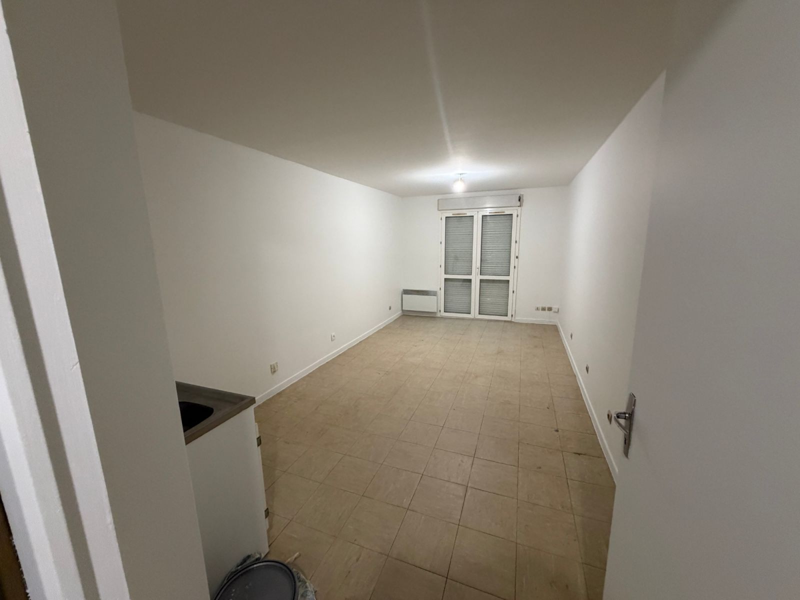Pièce principale du studio repeinte en blanc, sol carrelé beige et porte-fenêtre - Yvelines